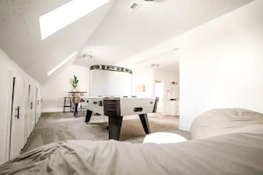 Ein Zimmer mit einem Bett, einem Kicker, einem Schreibtisch und einer Topfpflanze.