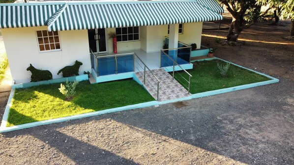 A two-story building with a green and white striped awning, a small porch, and a paved area with a metal railing. - Cozy Private Room near Border town Dajabón- Air Conditioner (Dajabón)