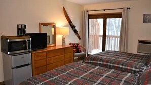 A bedroom with two beds, a microwave, a television, a dresser, and a window with curtains.