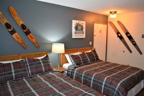 Ein Zimmer mit zwei Betten, einer Lampe, einer Tür und Skiern an der Wand.