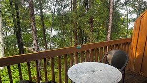 A wooden deck with a round table and two chairs, overlooking a forested area.