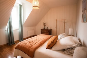 A bedroom with a sloped ceiling, a bed with a brown blanket, white pillows, a wooden dresser, and a bedside lamp.
