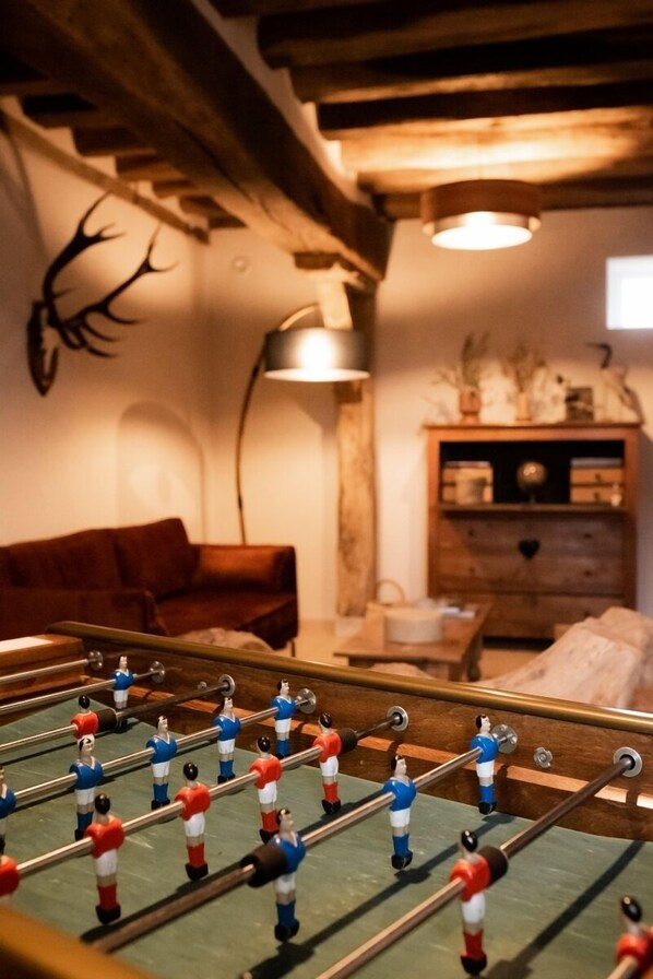 A cozy room with a foosball table, a brown leather sofa, a wooden cabinet, and a wall-mounted deer head.