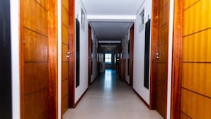 A long, narrow hallway with wooden doors on both sides, leading to a bright room at the end. - Economy HOTEL (Natal)