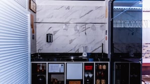 A kitchen with a marble backsplash, a stove, and a microwave. There is a window with a view of a fence. - Economy HOTEL (Natal)