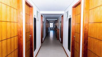 Um corredor comprido e estreito com portas de madeira em ambos os lados, que dá para um quarto iluminado no final.