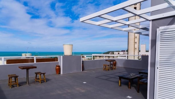 A rooftop terrace with tables and chairs, a water tank, and a view of the ocean. - Economy HOTEL (Natal)
