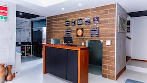 A modern reception desk with a wooden finish and black cabinets, surrounded by a tiled wall with various signs. - Economy HOTEL (Natal)
