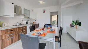 A modern kitchen with white cabinets, a stainless steel range hood, and a dining area with a glass table set for four. - La Perla Di Pianello, Pianello del Lario, Italy (Pianello del Lario)