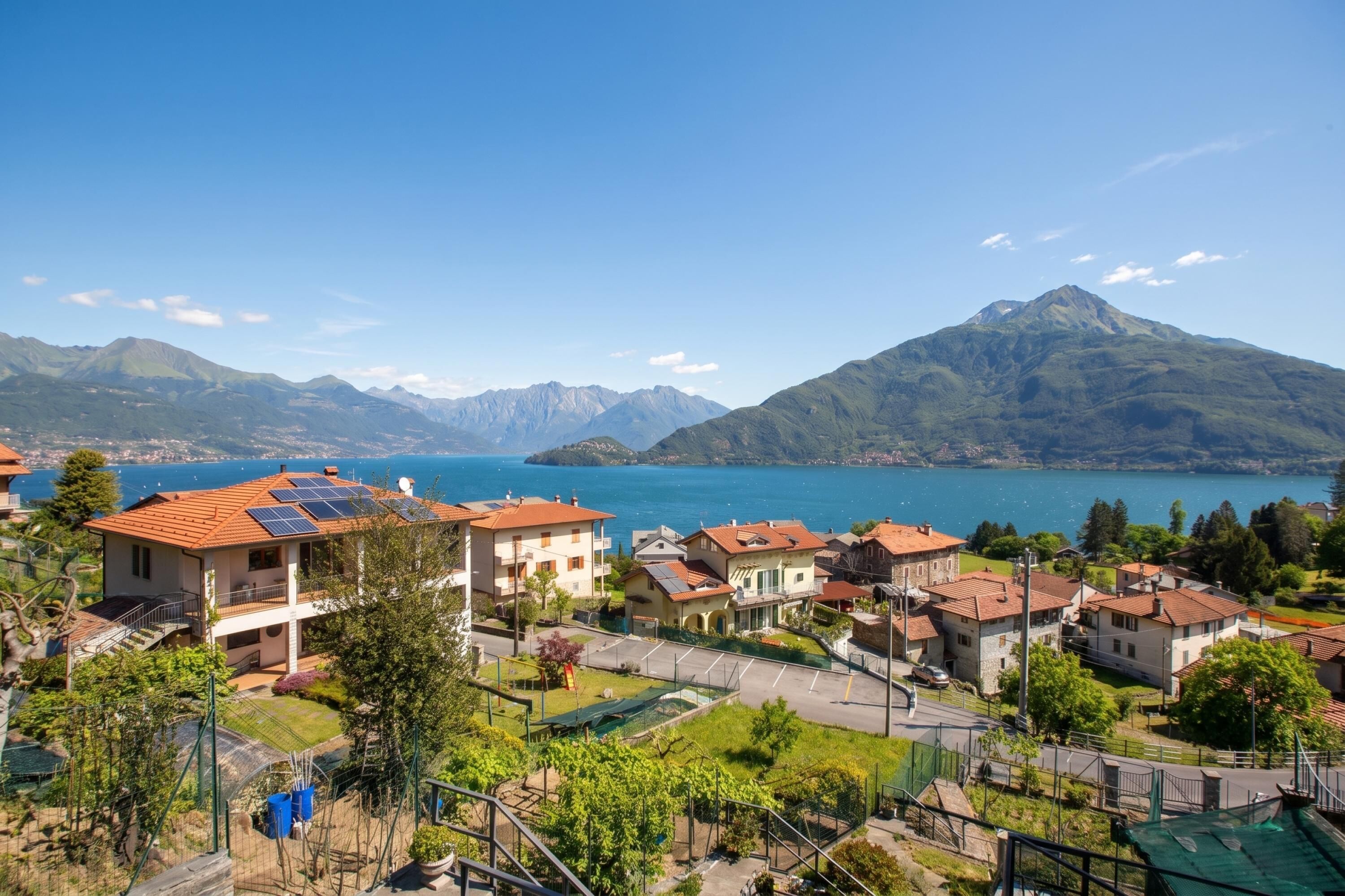 A residential area with houses, a clear blue sky, and a lake with mountains in the background.