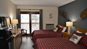 A hotel room with two beds, a desk with a coffee maker, a TV, and a sliding door to the balcony.
