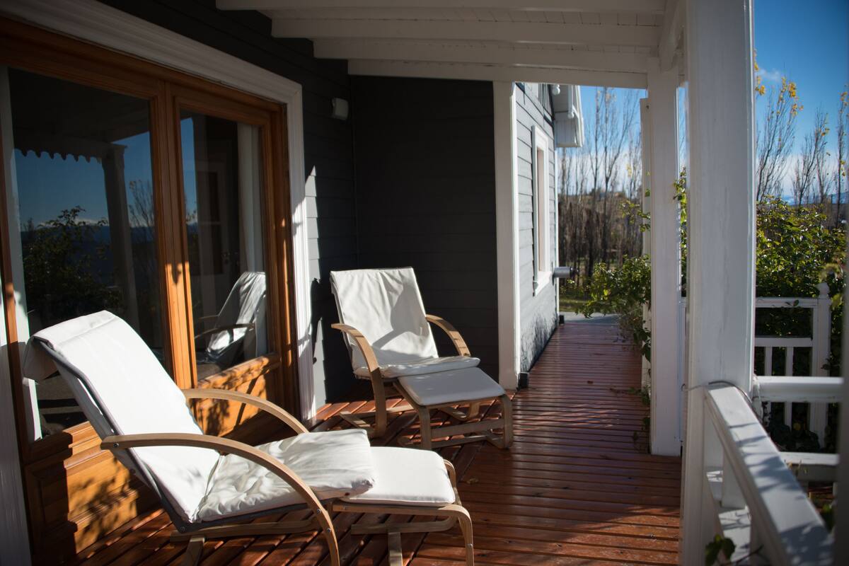 Una terraza de madera con dos sillas blancas acolchadas, una barandilla blanca y vistas del paisaje circundante.