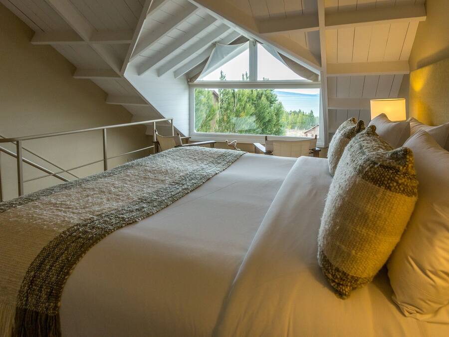 Un dormitorio con una cama grande, vistas a árboles a través de una ventana y una escalera.