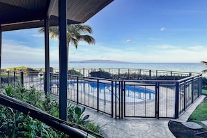 A pool area with a view of the ocean and a mountain in the distance.