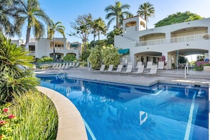 A swimming pool with lounge chairs and palm trees, surrounded by buildings with balconies. - Palms at Wailea 703 - Modern Renovation, Prime Location, Full AC, Close to Pool! (Kihei)