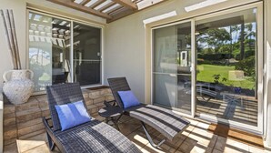 A covered patio with two wicker lounge chairs and a large sliding glass door leading to a garden. - Palms at Wailea 703 - Modern Renovation, Prime Location, Full AC, Close to Pool! (Kihei)
