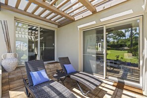 Eine überdachte Terrasse mit zwei Korlounge-Stühlen und einer großen Schiebeglastür, die zu einem Garten führt.