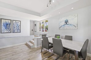 Un comedor moderno con una mesa blanca y sillas grises, una escalera que lleva a otra habitación y obras de arte en las paredes.