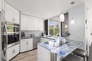 A modern kitchen with white cabinets, stainless steel appliances, and a marble island.