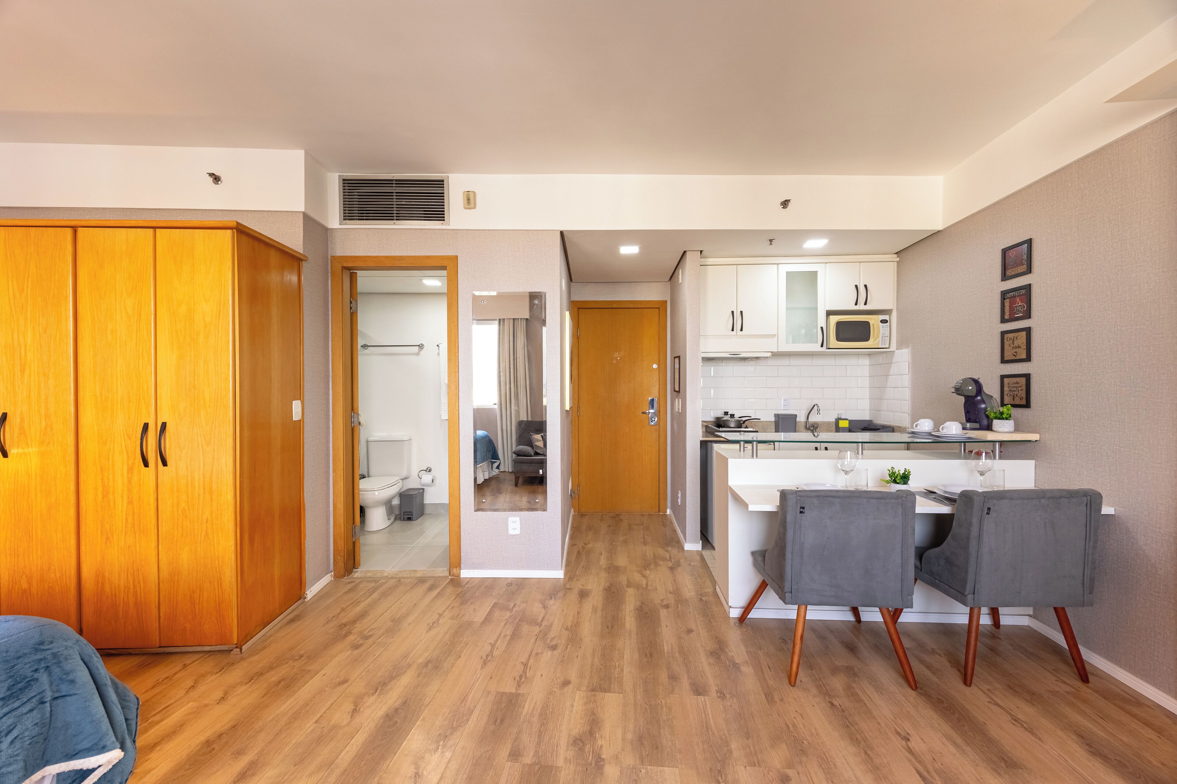 A modern kitchen with wooden cabinets, a microwave, and a dining area with two grey chairs.