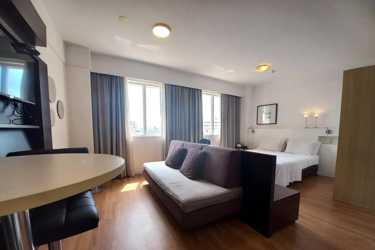 Hotellihuone, jossa on sänky, sohva, ruokapöytä ja televisio.