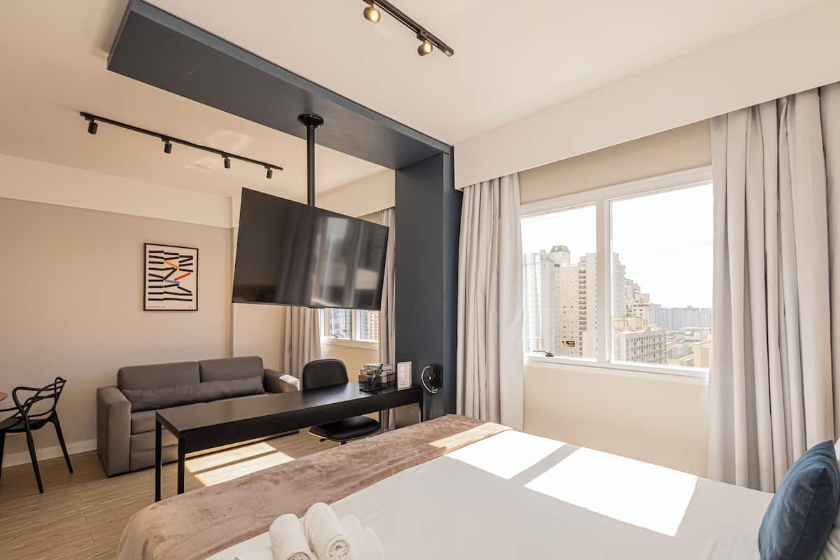 Moderni hotellihuone, jossa on suuri sänky, työpöytä, sohva ja televisio.