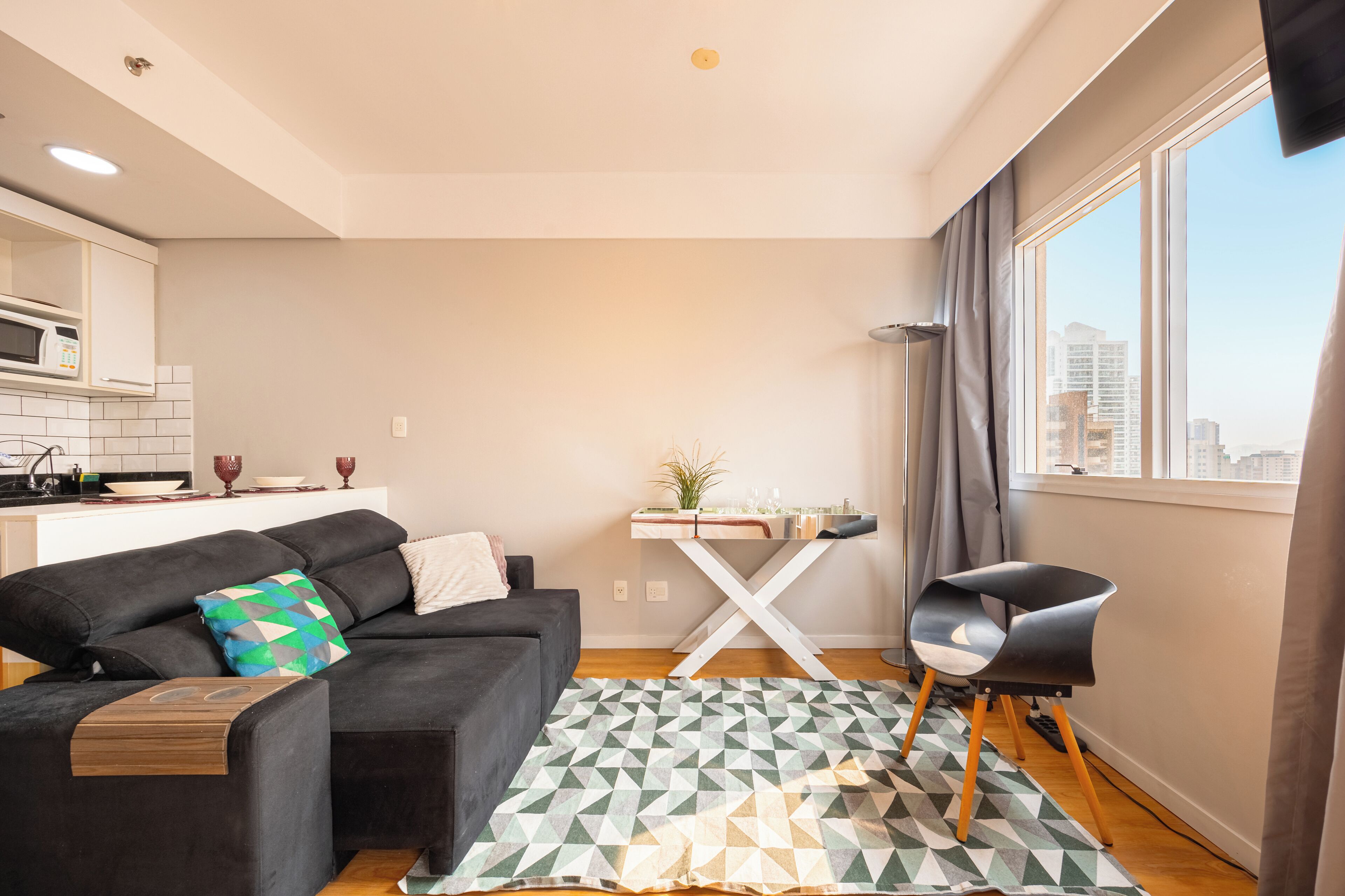 A modern living room with a black sofa, a geometric patterned rug, a dining table with a plant, and a city view through large windows.