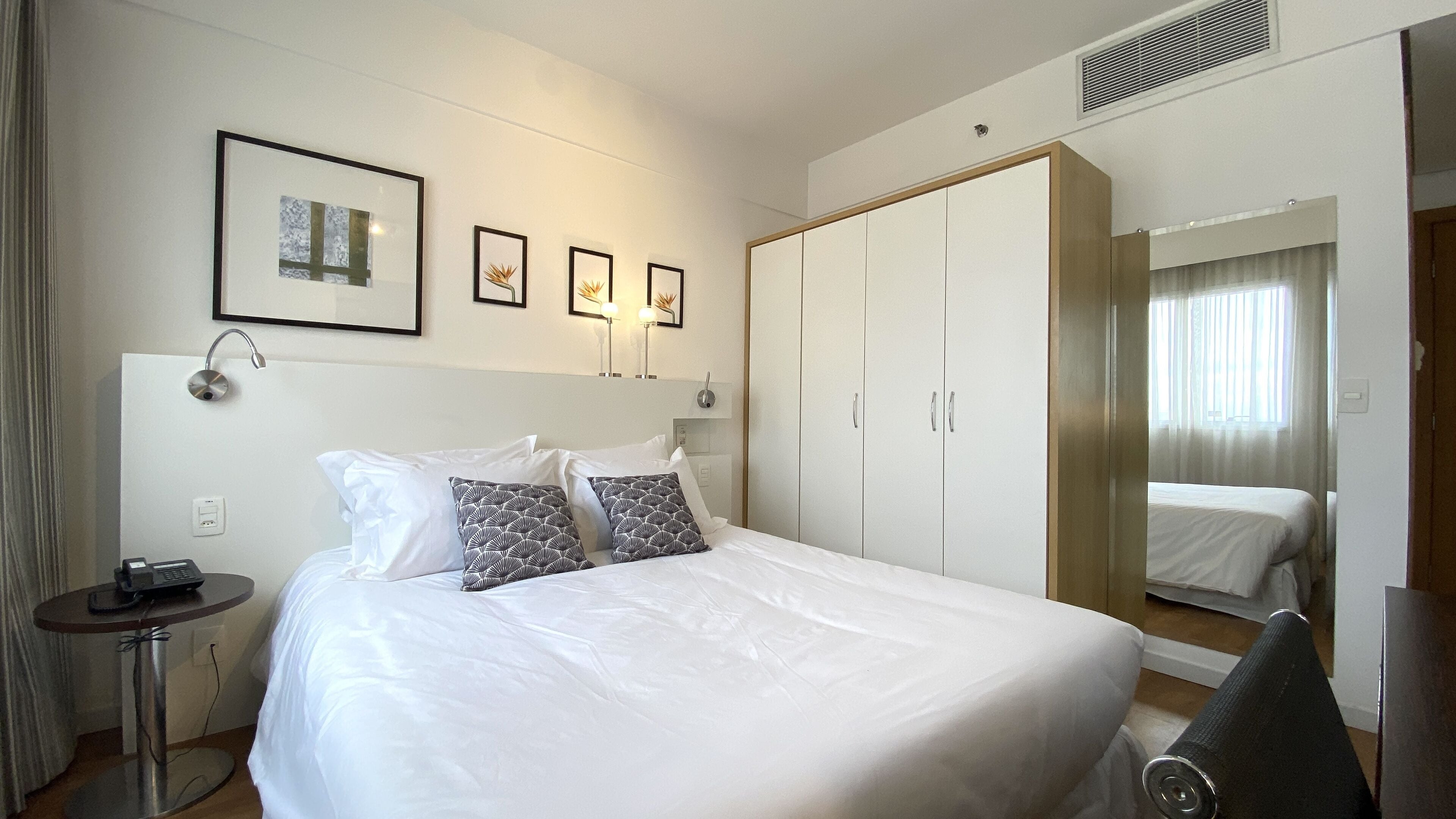 A hotel room with a large bed, a bedside table with a phone, and a wardrobe with sliding doors.