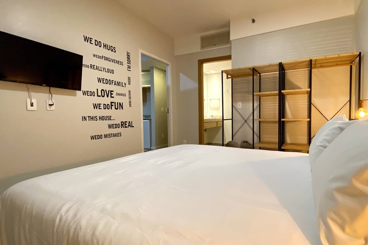 Hotellihuone, jossa on suuri sänky, peilillä varustettu vaatekaappi ja seinä, jossa on kannustavia sitaatteja.
