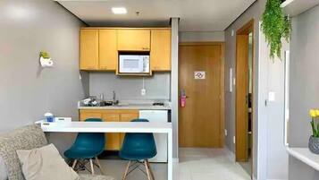 A compact kitchen with a microwave, a sink, and a countertop. There is a sofa with a cushion and two blue chairs. A door leads to another room.