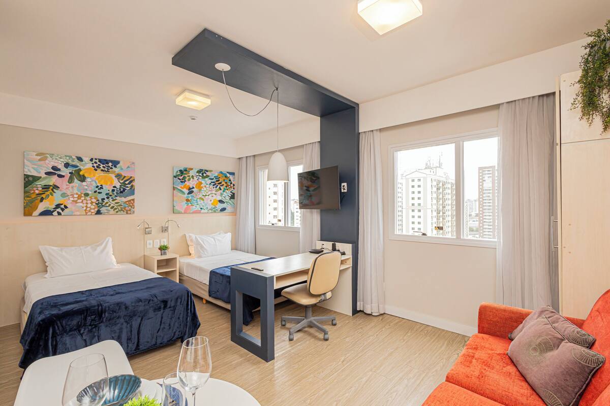 Hotellihuone, jossa on kaksi sänkyä, työpöytä, televisio ja sohva.