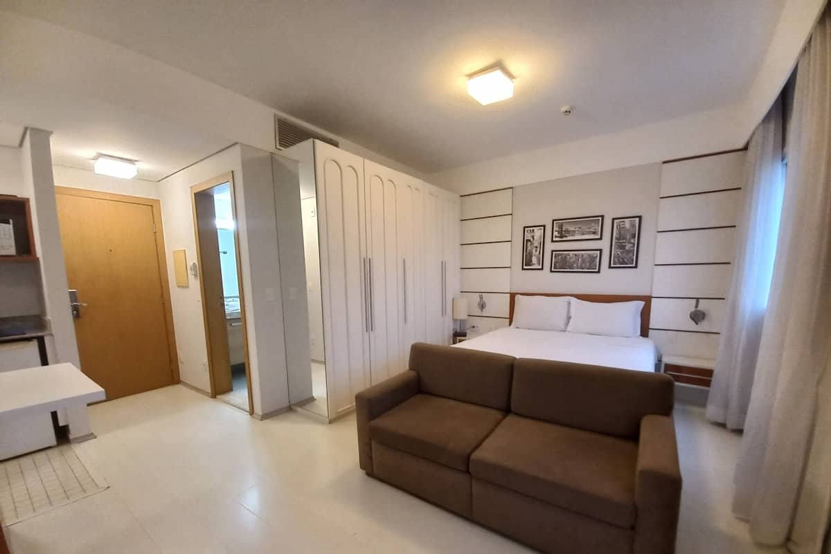 Hotellihuone, jossa on sänky, ruskea sohva, vaatekaappi ja työpöytä.