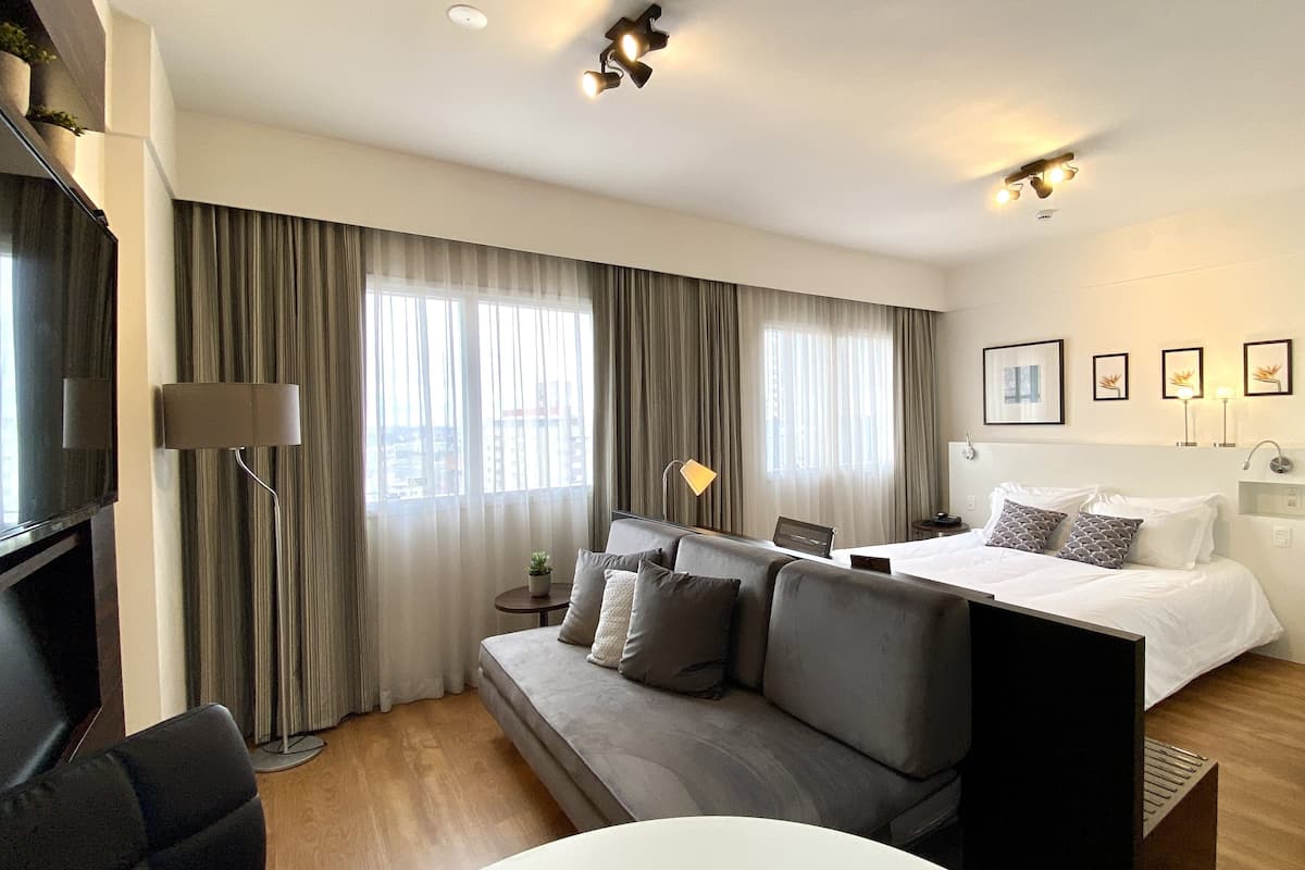Moderni hotellihuone, jossa on sänky, sohva, televisio ja työpöytä.