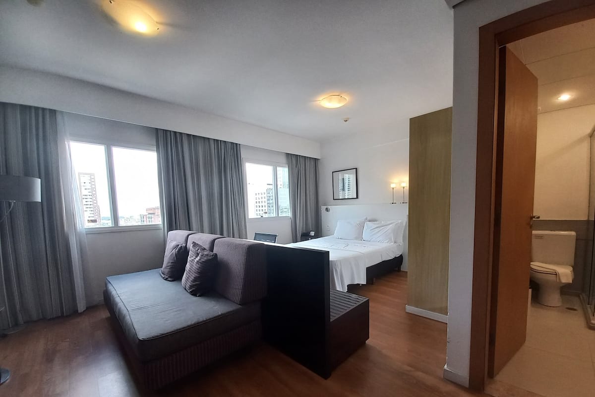 Moderni hotellihuone, jossa on sohva, sänky, työpöytä ja kylpyhuone, joka näkyy avoimesta ovesta.