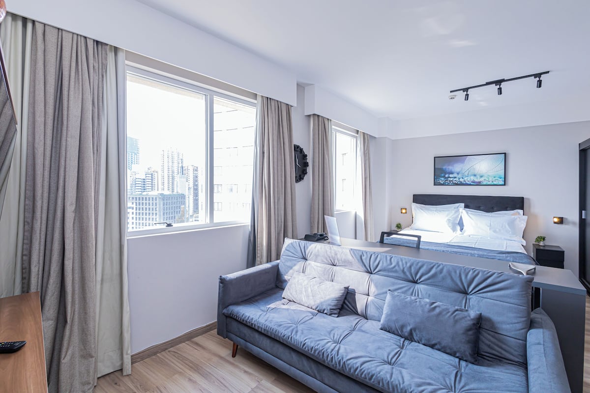 Moderni hotellihuone, jossa on suuri sänky, sohva, työpöytä ja näkymä kaupunkiin.