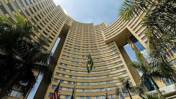 Un edificio de hotel alto y curvo con varios pisos, que presenta una destacada bandera estadounidense, una bandera brasileña y un letrero que dice "Comfort Suites".