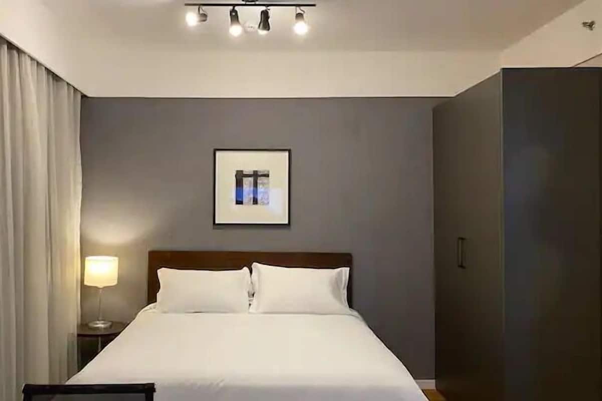 Hotellihuone, jossa on suuri sänky, yöpöytä lampun kanssa, seinällä oleva kehystetty taulu ja ikkuna, jossa on verhot.