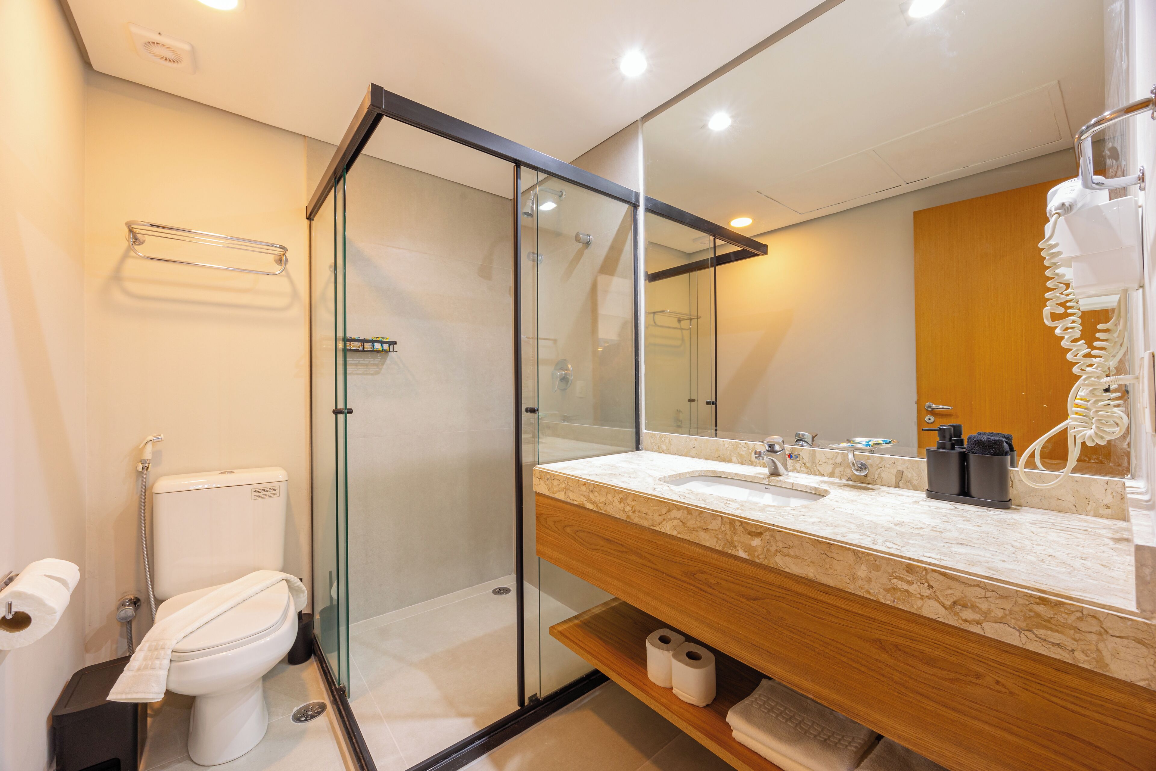 Un baño moderno con ducha envuelta en vidrio, tocador de madera y un espejo grande.