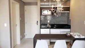 Una cocina moderna con encimera oscura, sillas blancas y una araña.