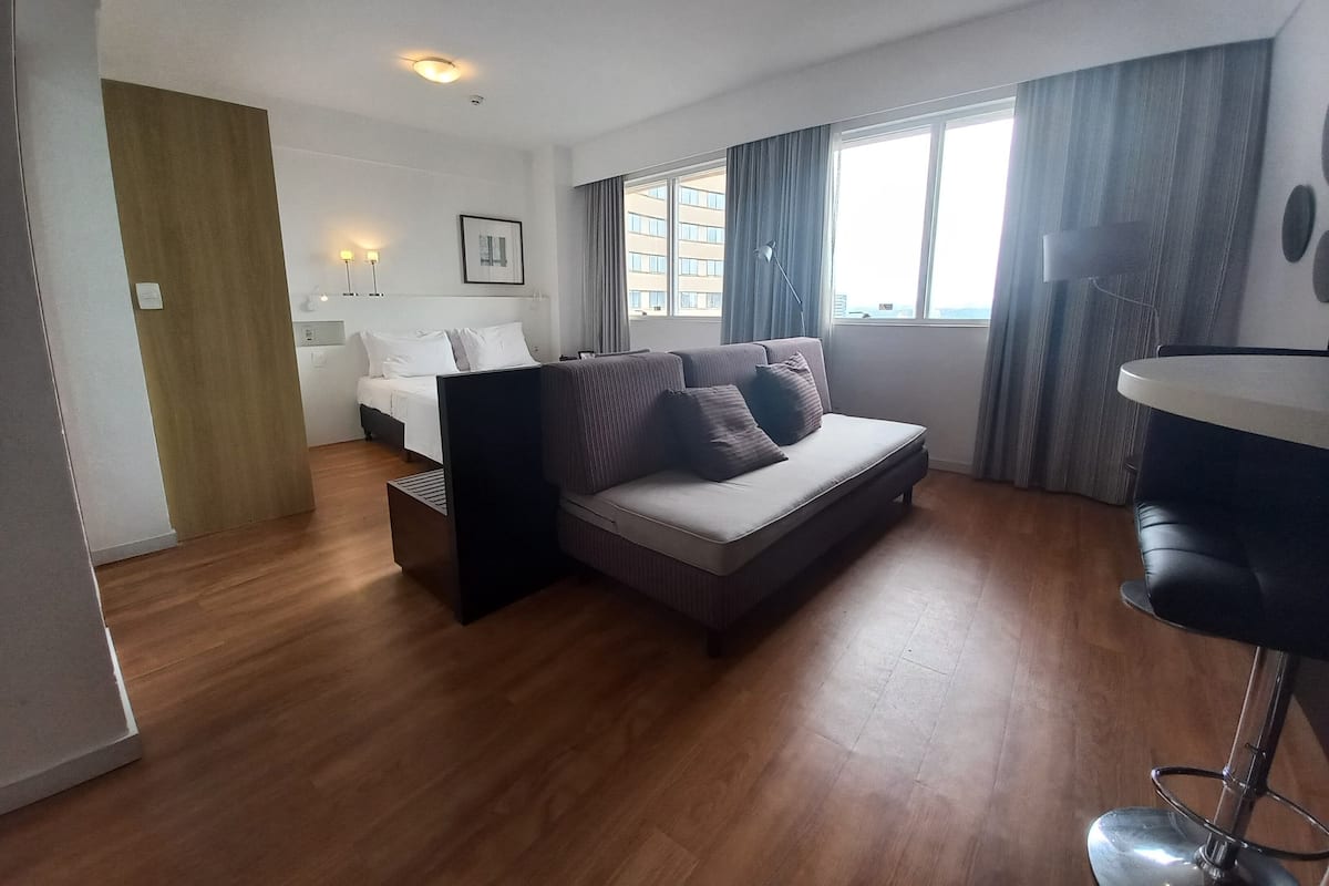 Moderni hotellihuone, jossa on sänky, sohva ja pieni baaritiski.