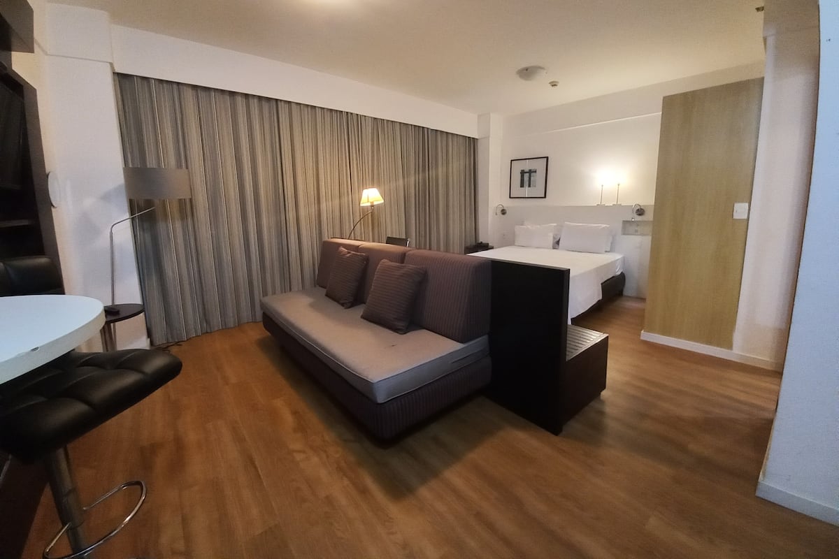 Moderni hotellihuone, jossa on sohva, pieni pöytä, sänky ja työpöytä.