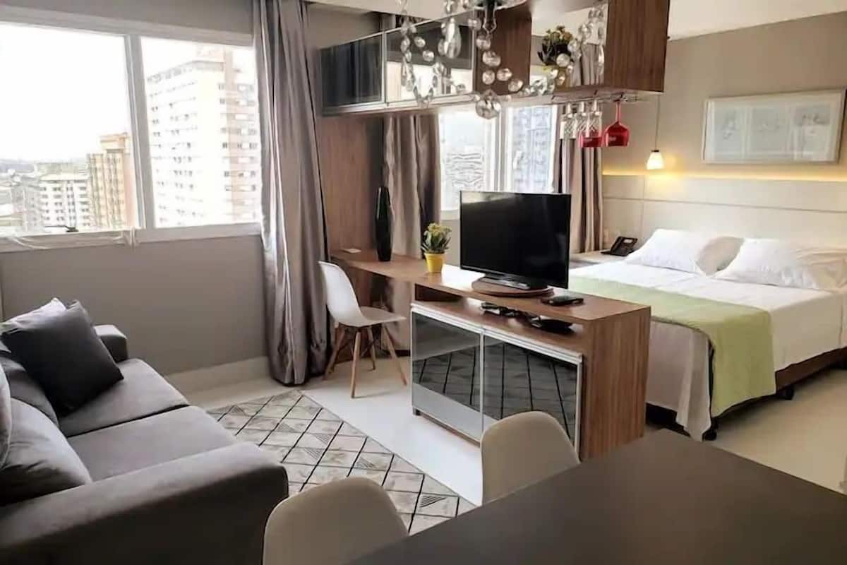 Moderni hotellihuone, jossa on sänky, työpöytä ja televisio, sohva sekä näkymä kaupunkiin.
