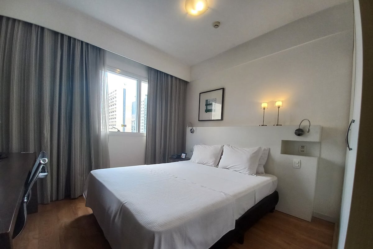 Hotellihuone, jossa on suuri sänky, työpöytä ja ikkuna, jossa on verhot.