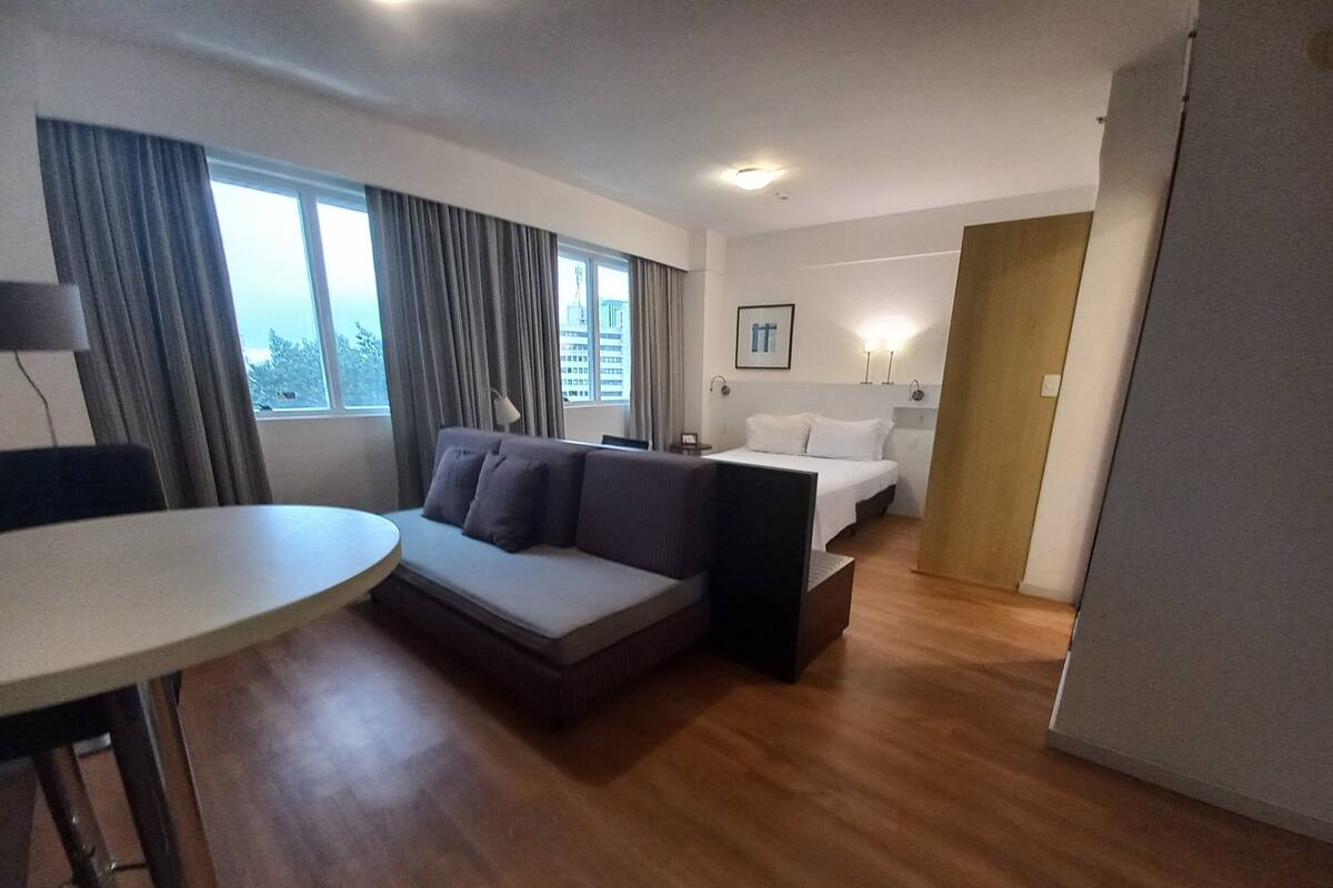 Moderni hotellihuone, jossa on sohva, sänky, ruokapöytä ja näkymä kaupunkiin.