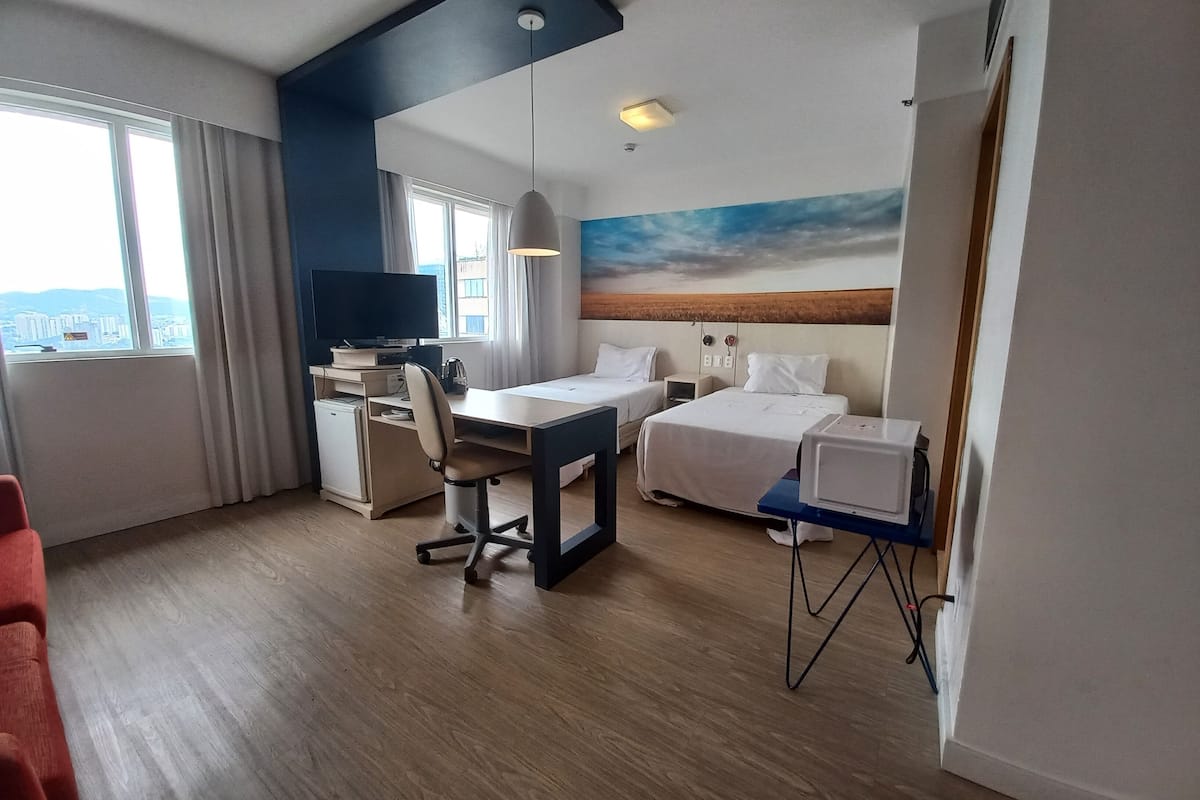 Hotellihuone, jossa on työpöytä, kaksi sänkyä, televisio ja näkymä kaupunkiin.