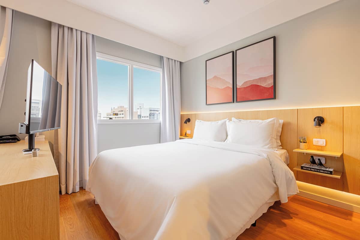 Moderni hotellihuone, jossa on suuri sänky, työpöytä, televisio ja ikkuna, jossa on verhot.