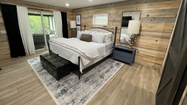 Un dormitorio con cama, mesitas de noche, un espejo y una ventana con cortinas.