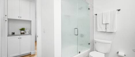 A modern bathroom with a glass shower enclosure, a toilet, and a sink area with cabinets.