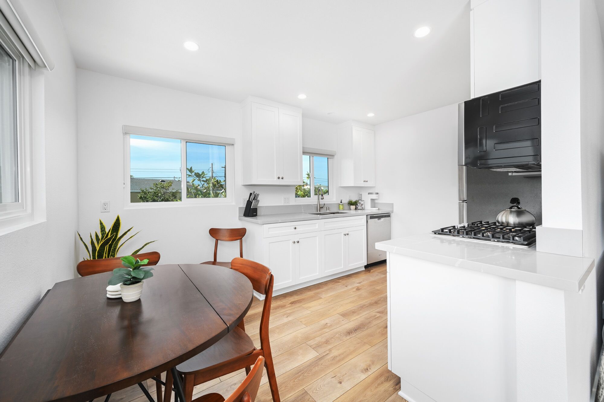 A modern kitchen with white cabinetry, a wooden dining table, and a gas stove.
