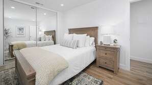 A bedroom with a large bed, a nightstand, a mirror, and a wooden floor.